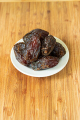 Big pitted dried dates on a small white plate set on a wooden boar top view