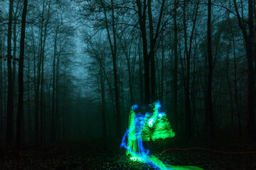 Blue and green lights moving in mysterious dark and foggy forest at night