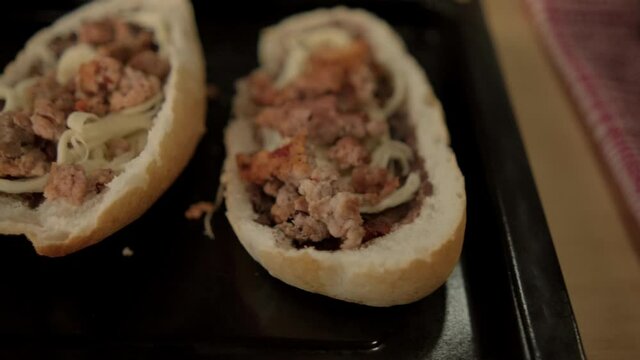 Blue tongs adding chopped meat to traditional Mexican molletes above black tray
