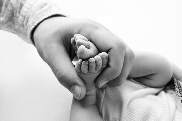 The father holds the bare feet of the newborn on a white background. Tiny legs in the hands of a man. Family, parents and homework concept. Health care, pediatrics. Black and white photography.