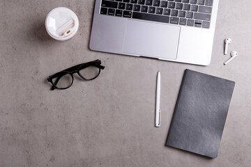Cropped shot of minimalistic workspace. Tabletop of concrete textured desk with metallic grey laptop. Workplace of a developer concept. Background, copy space for text, flat lay, close up, top view.