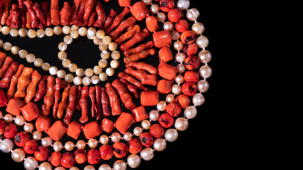 Shiny red coral and iridescent white pearl necklaces are  laid out in circles on a black...