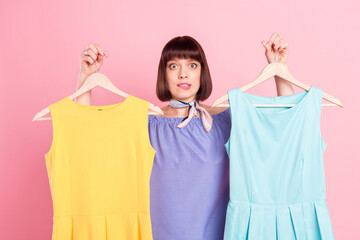 Photo portrait woman fitting clothes shopping unsure compare dresses doubt unsure bite lip isolated pastel pink color background