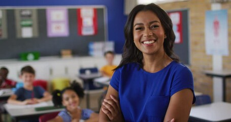 Portrait of happy mixed race female teacher standing in classroom with children in background - Powered by Adobe
