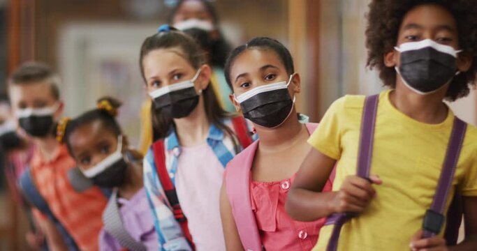 Diverse schoolchildren standing in queue, all wearing face masks