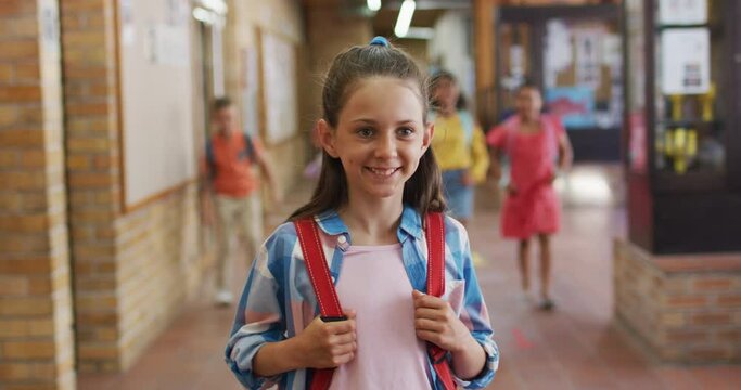 Portrait of happy caucasian schoolgirl standing in corridor looking at camera