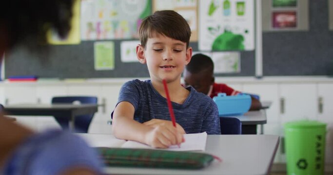Portrait of happy caucasian schoolboy sitting at classroom, making notes, looking at camera