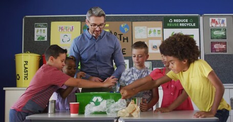 Diverse teacher and schoolchildren standing in classroom learning about recycling trash