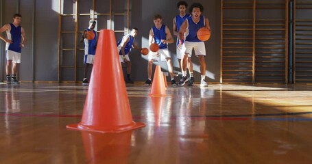 Diverse male basketball team wearing blue sportswear practice dribbling ball