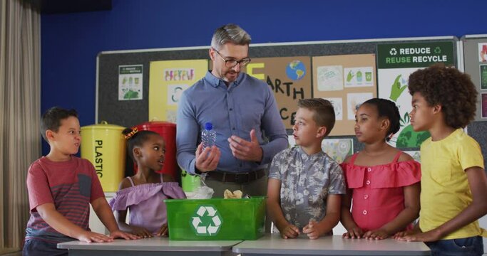 Diverse teacher and schoolchildren standing in classroom learning about recycling trash