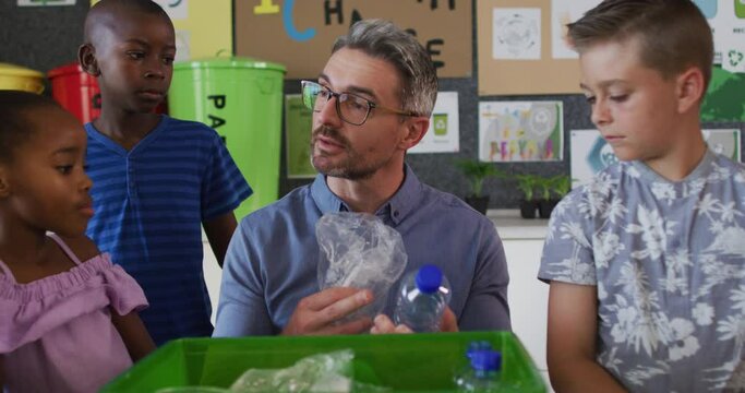 Diverse teacher and schoolchildren standing in classroom learning about recycling trash