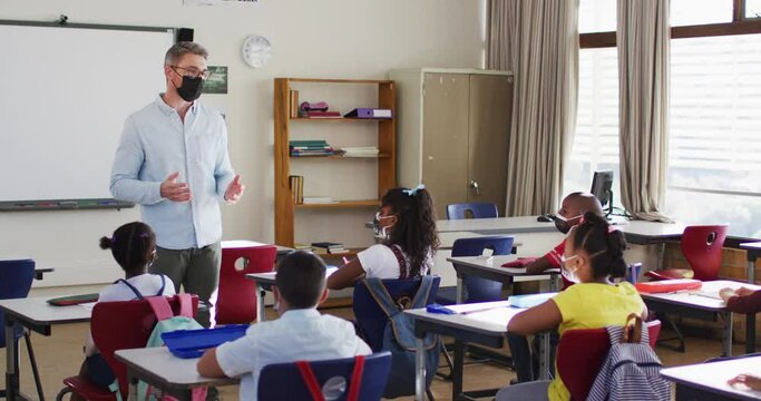 Caucasian male teacher wearing face mask teaching students in the class at school