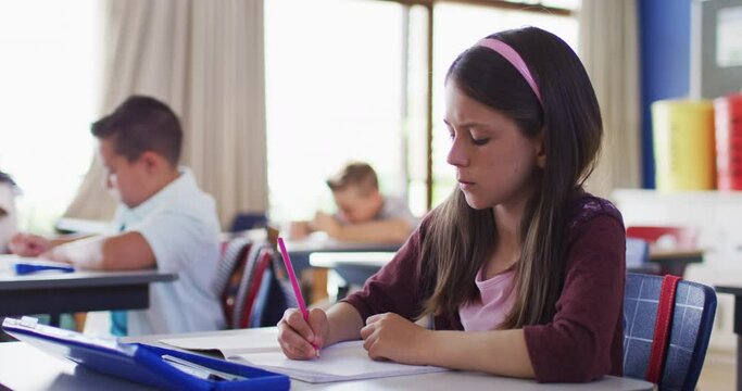 Portrait of caucasian schoolgirl sitting in classroom, making notes