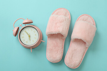 Alarm clock and slippers on blue background