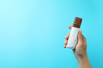 Female hand holds tasty candy bar on blue background