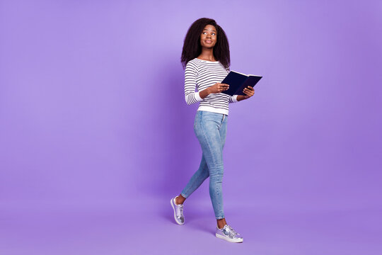 Full length profile side photo of young black girl happy smile go walk look empty space hold book isolated over violet color background