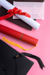 Graduation academic cap with diploma and mask isolated on pink table background.
