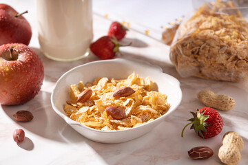 Closeup of bowl of ccrispy cornflakes,nuts,fruits and bottle of milk on the table.Sunny morning and tasty breakfast