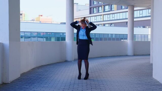 A woman in office clothes is dancing on the background of a modern building. An excited young business woman is celebrating success or the end of the working day