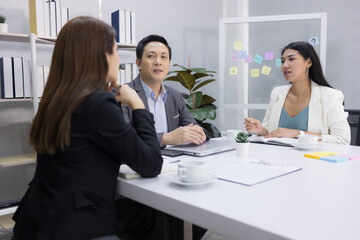 Motivated middle-aged Asian businessman and two young businesswomen happily exchanged ideas for business plans, enjoying working together at the office. leadership workplace.