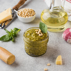 Pesto sauce in a jar with a piece of parmesan cheese, basil leaves, pine nuts and olive oil in a bottle. Italian cuisine