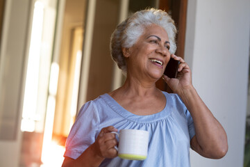 Mixed race senior woman drinking coffee and talking on smartphone