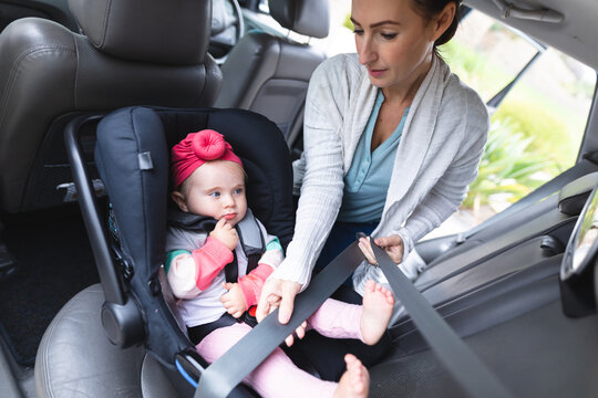 Caucasian mother putting her baby in safety baby seat in the car