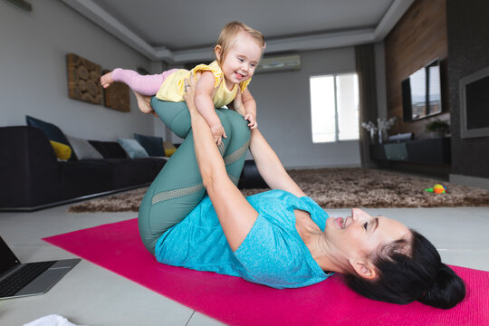Caucasian mother holding her baby and doing yoga at home