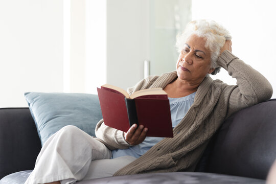 Mixed race senior woman sitting on sofa reading book