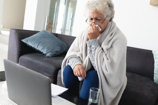 Mixed race senior woman sitting on sofa making video call using laptop