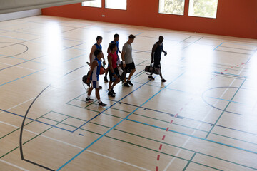 Diverse male basketball team and coach leaving gym after match