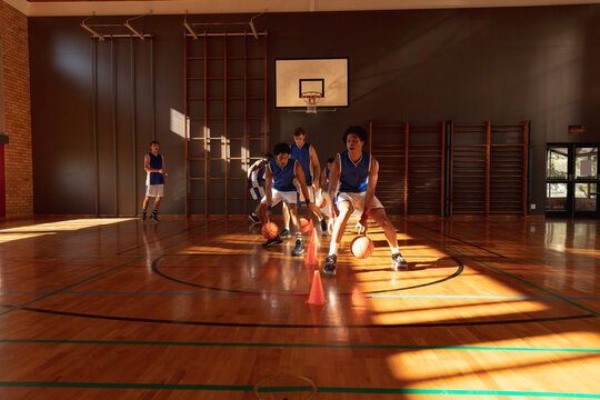 Diverse male basketball team wearing blue sportswear and practice dribbling ball - Powered by Adobe