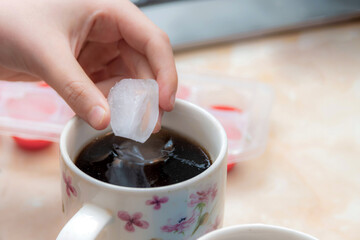 The girl throws ice into the mug to cool the drink.