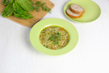 Noodles with chicken broth and dill in green plate on white background