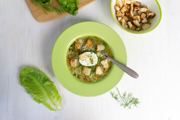 Noodles with chicken broth, egg, spoon and dill in green plate on white background