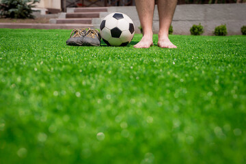 Legs of unrecognizable barefoot football player against artificial grass. Soccer ball, street...