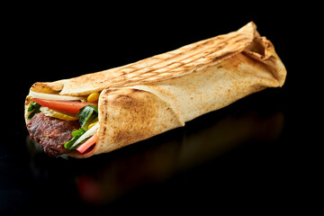 Appetizing shawarma with mutton lula kebab, cucumbers, carrots and tomatoes in pita bread. Black...