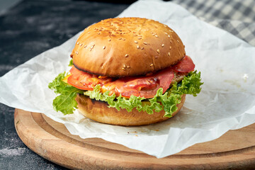 Delicious burger with chicken, tomatoes, lettuce, cucumber melted cheese on white parchment. Dark background. American fast food. Chickenburger