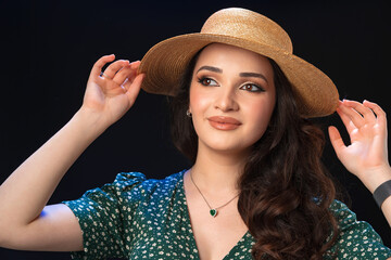 Beautiful young woman with straw hat posing against black background