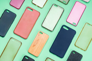 Pile of multicolored plastic back covers for mobile phone. Choice of smart phone protector accessories on green background. A lot of silicone phone backs or skins next to each other