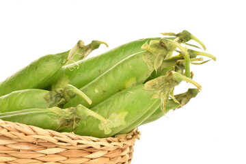 Several organic green pea pods in a straw plate, close-up, isolated on white.