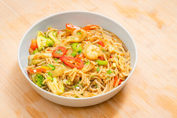 Golden coloured spicy sea food noodles with shrimp, broccoli, chilli pepper in a plate on wooden table