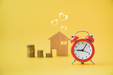red analog clock ,blurred stack of coins and brown paper with heart shape on yellow background ,...