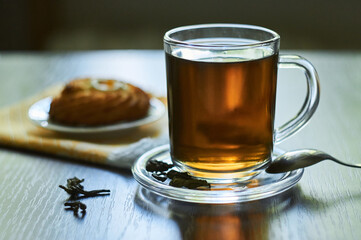 Herbal tea in glass cup with cookie on a white small plate on a dark wooden surface