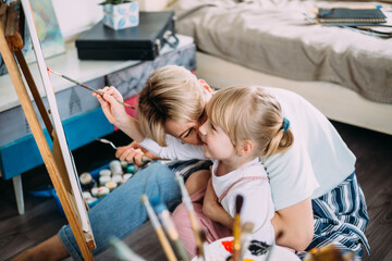 beautiful mother artist and her child paint picture at home with acrylic paints.