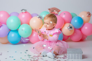 baby girl celebrates birthday on white background catching confetti balloons