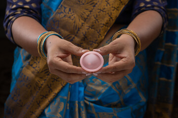 An Indian woman holding reusable silicon Menstrualcup and showing  different types of folding,