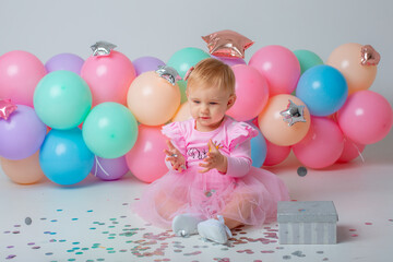Fototapeta na wymiar baby girl celebrates birthday on white background catching confetti balloons
