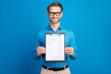 Photo of young man happy positive smile show clipboard papers documents isolated over blue color background