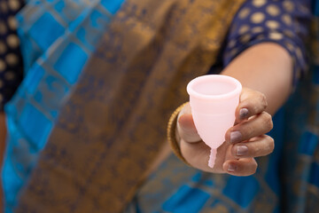 An Indian woman holding reusable silicon Menstrualcup and showing  different types of folding,